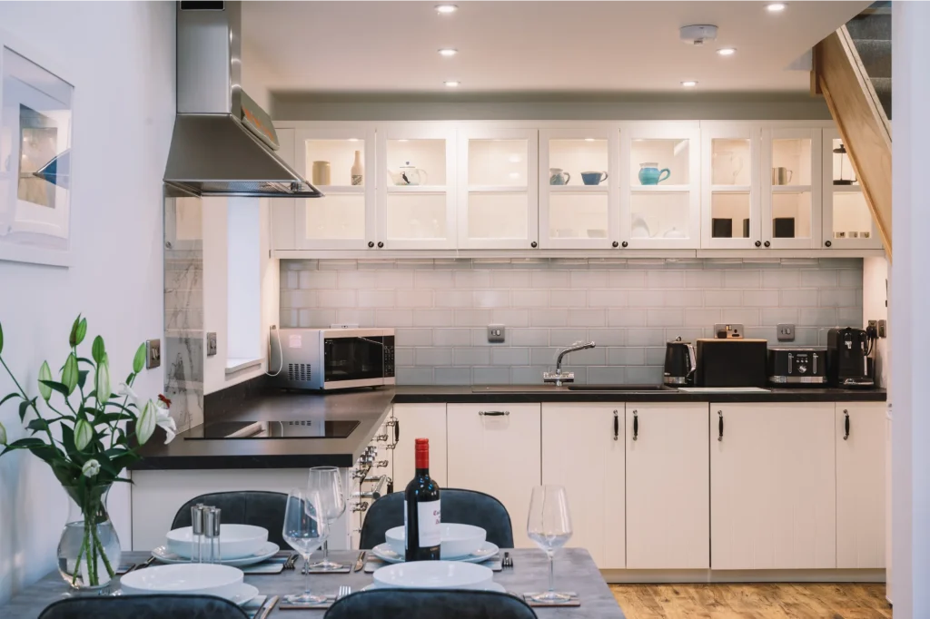 An Iolaire full size fitted kitchen with dining area beside it and a view of the mezzanine above. Kitchen has oven, hob, steel extractor fan, window, microwave, kettle, toaster, coffee machine, floor and wall cupboards and lots of lighting