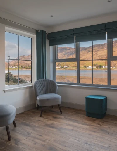 An Iolaire spacious atrium with two easy chairs, plus teal velvet stool and wide, open views onto the sea and the hills beyond