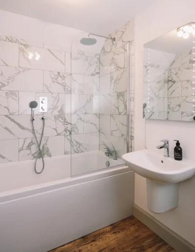 An Iolaire luxury bathroom, with marble style tiling, full size bath, rain shower and hand held shower and Highland Soap company toiletries